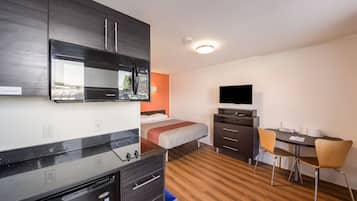 A hotel room with a bed, a desk with a chair, a television, a microwave, and a built-in oven.