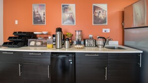 Une cuisine avec un plan de travail blanc, des meubles noirs et un lave-vaisselle. Trois affiches encadrées ornent le mur, et une machine à café est posée sur le plan de travail.