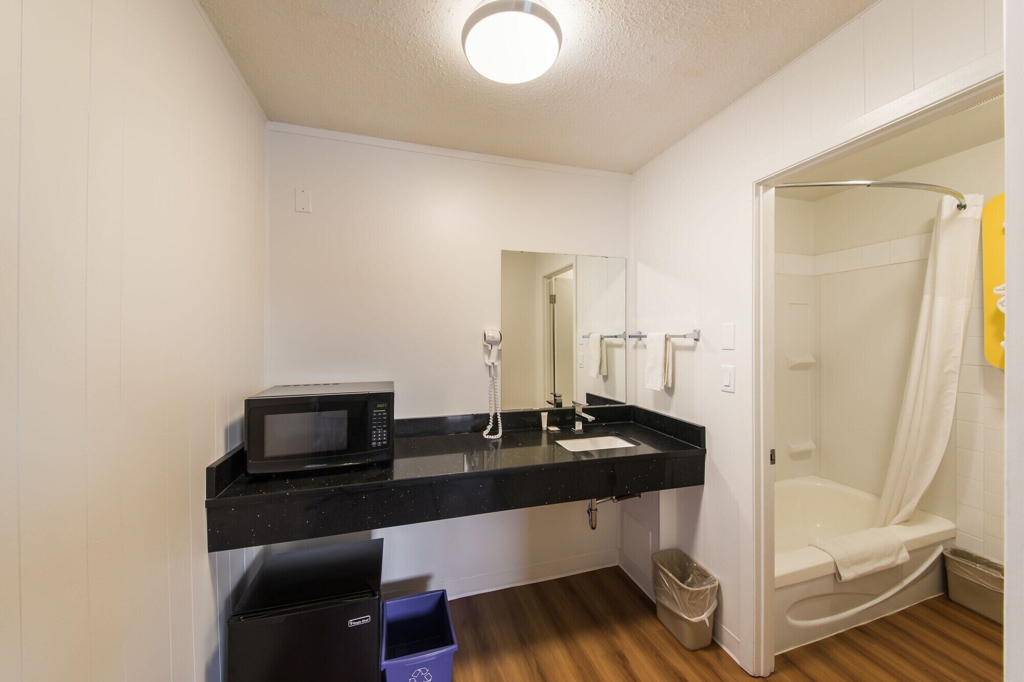 A modern bathroom with a black countertop, a white sink, a mirror, a shower, and a toilet.