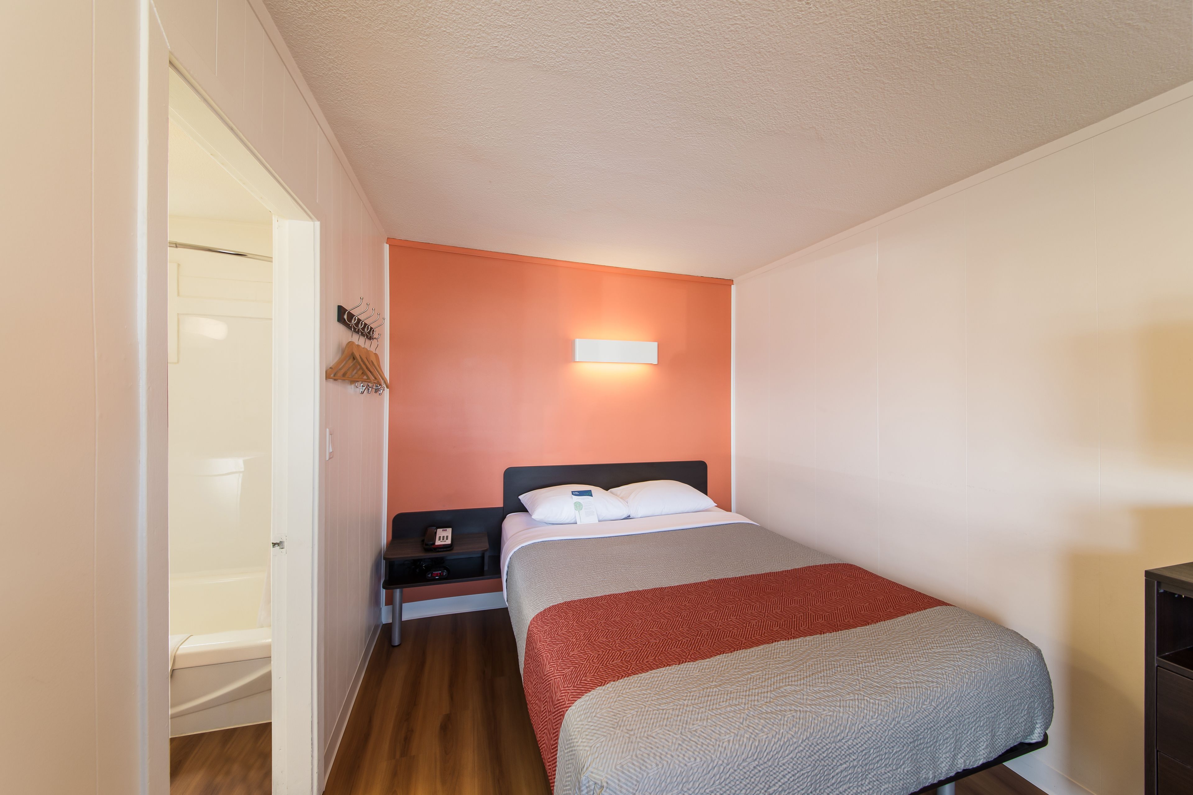 Ein kleines, kompaktes Schlafzimmer mit einem Einzelbett, einem Nachttisch, einer Wandleuchte und einer Tür zu einem Badezimmer.