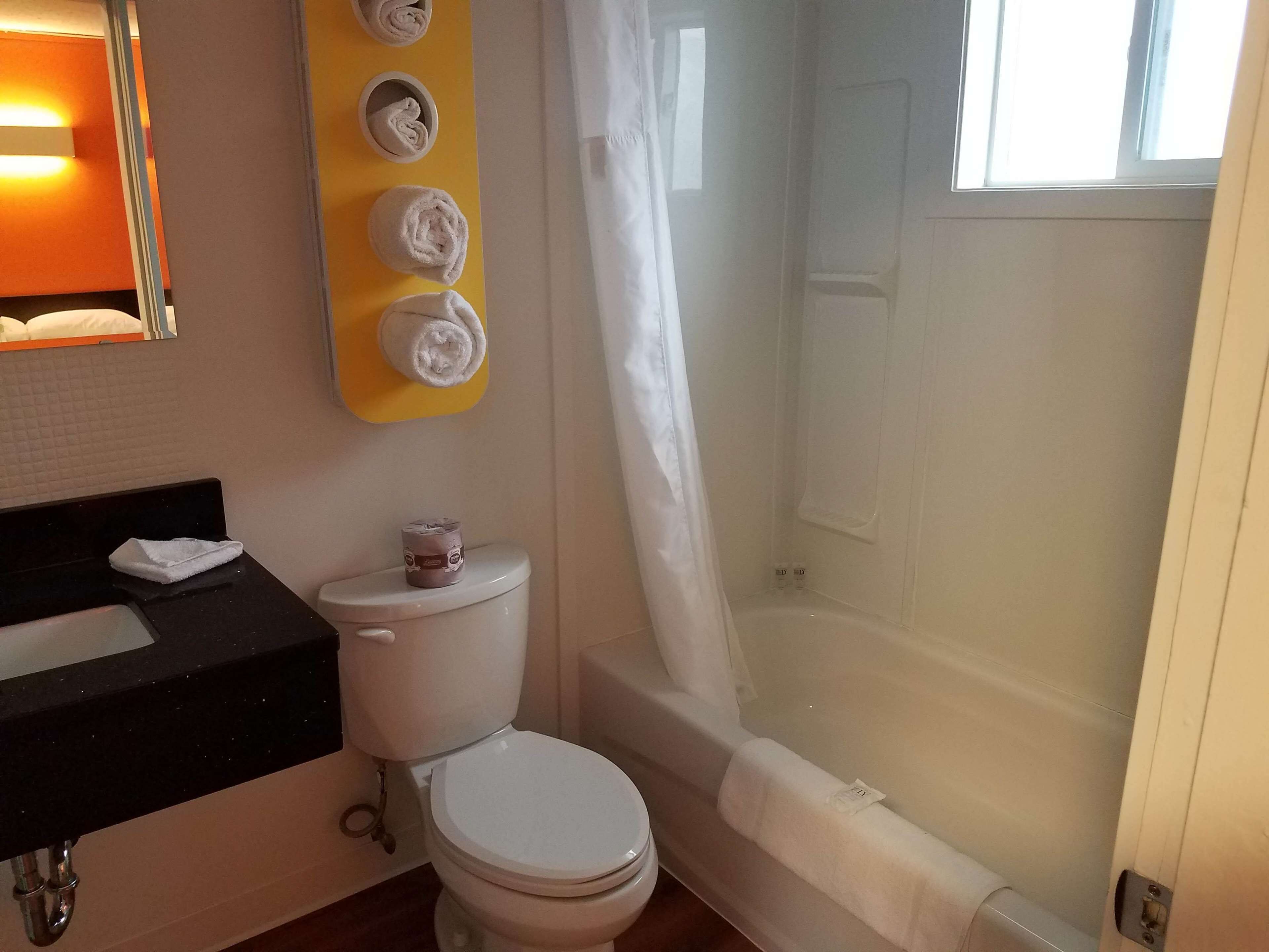 Une salle de bain avec des toilettes, un lavabo et une baignoire. Des serviettes sont suspendues sur un porte-serviettes jaune.