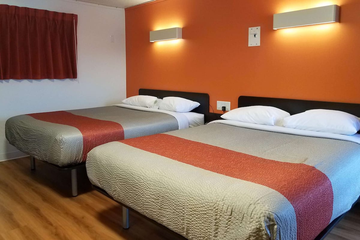 Habitación de hotel con dos camas, cada una con una manta roja y gris, y una cortina roja en la ventana.