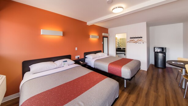 Une chambre d’hôtel avec deux lits, un bureau, une chaise, un réfrigérateur et un miroir.