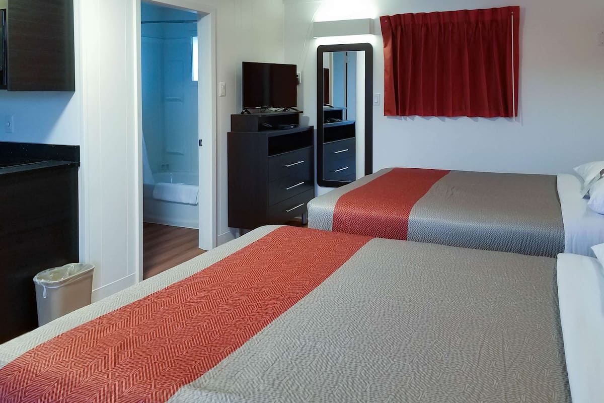Habitación de hotel con dos camas, un televisor, un armario y un baño visible a través de una puerta abierta.