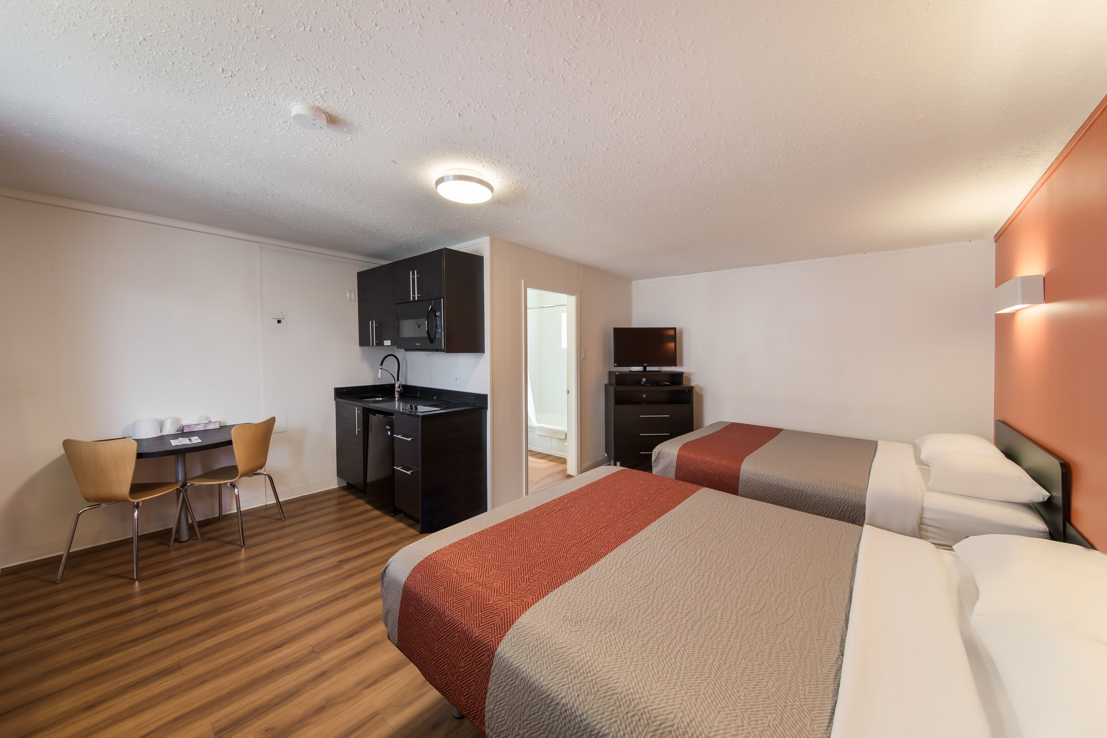 A hotel room with two beds, a kitchenette, a dining area with a table and chairs, and a television.