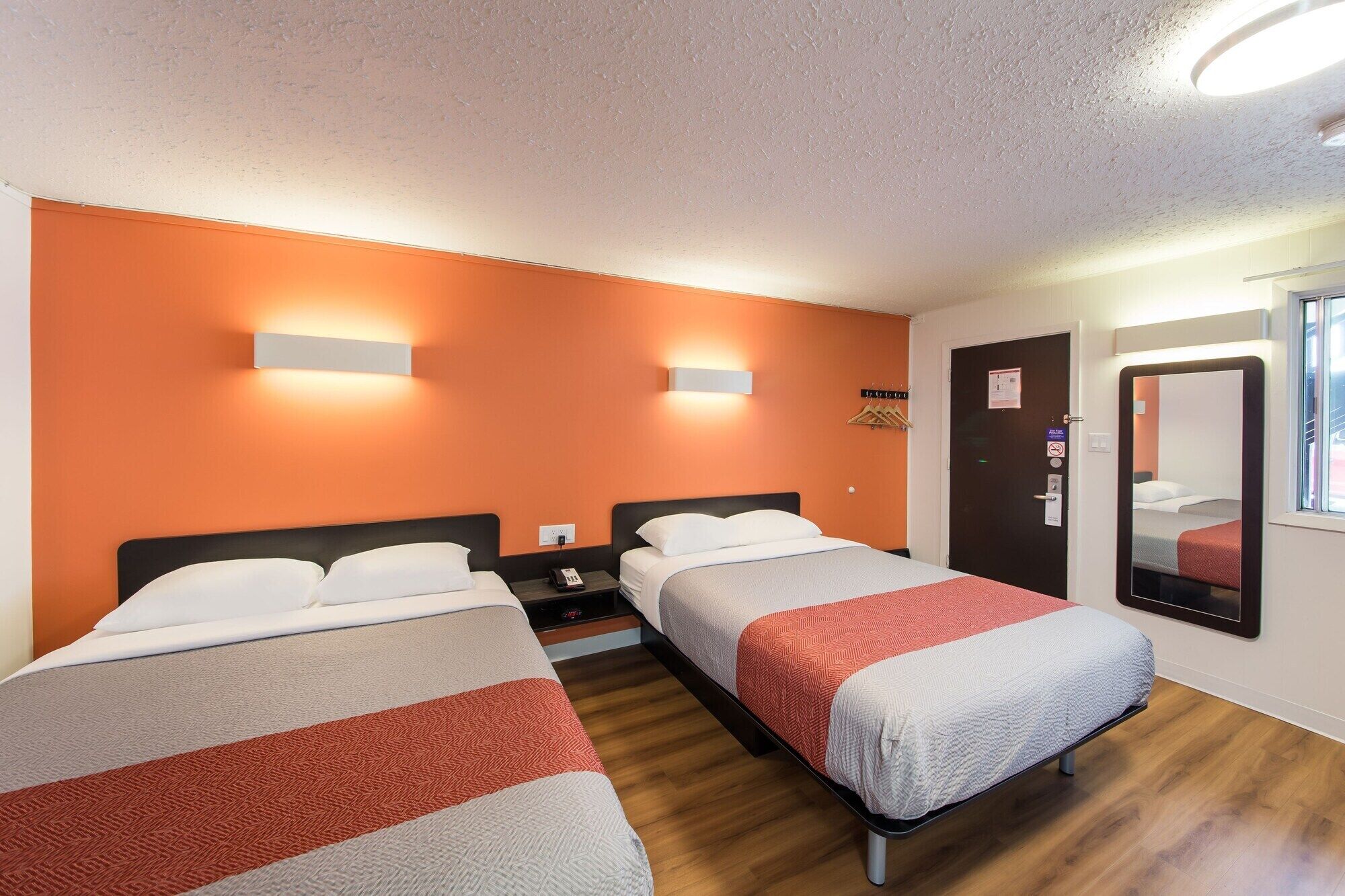 Une chambre d’hôtel avec deux lits, des murs orange et un plancher en bois.