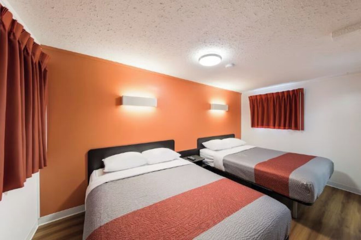 Ein Hotelzimmer mit zwei Betten, einem roten Vorhang, einer Leuchte und einer Wandlampe.
