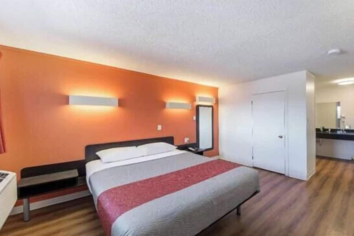 Habitación de hotel con cama, escritorio, espejo y kitchenette.