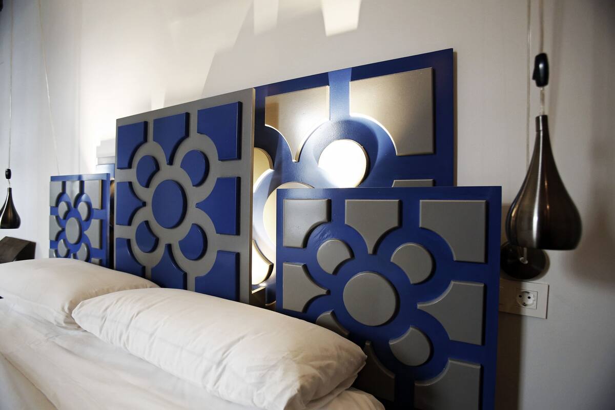 A bedroom with a bed, a wall-mounted light fixture, and a power outlet.