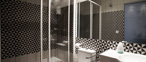 A modern bathroom with a glass-enclosed shower, a toilet with a grab bar, and a sink with a mirror.