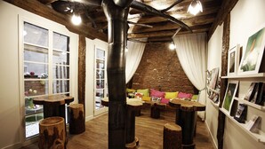 A cozy room with wooden floors, a large black pipe, and a brick wall. There are wooden stools and a sofa with cushions. - Pensión Basque Boutique (Bilbao)