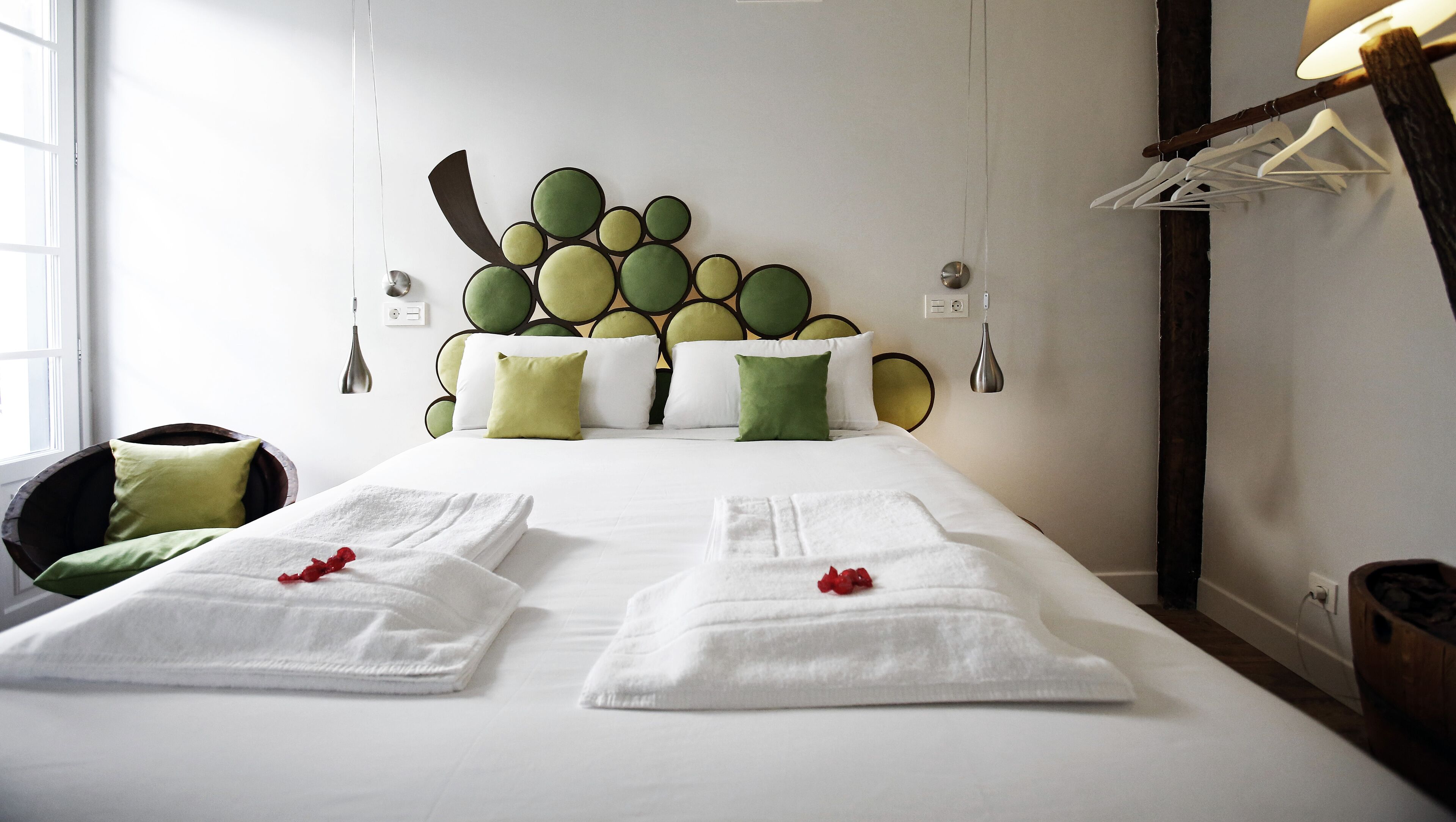 A hotel room with a bed, two towels, a chair, and a wall with a circular pattern.
