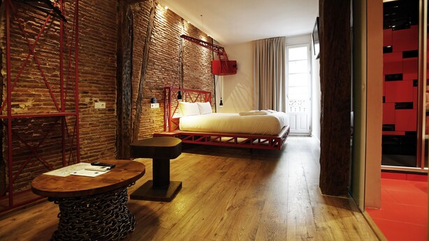 A hotel room with a brick wall, a bed with white linens, a wooden table, and a red metal ladder. - Pensión Basque Boutique (Bilbao)
