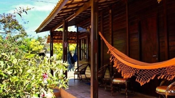 A wooden building with a covered porch, outdoor seating, and a hammock. - Pousada Ares de Noronha (Fernando de Noronha)