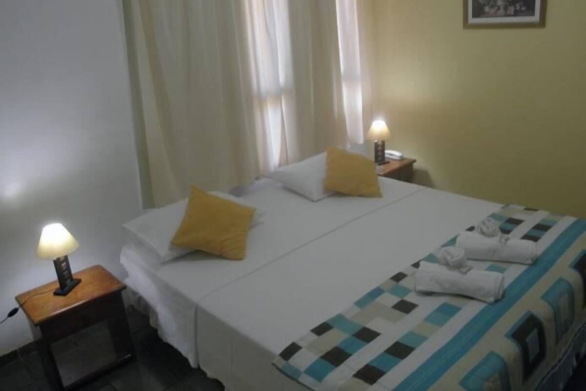 Une chambre d’hôtel avec un lit, deux oreillers, une table de chevet avec une lampe et un tableau accroché au mur.