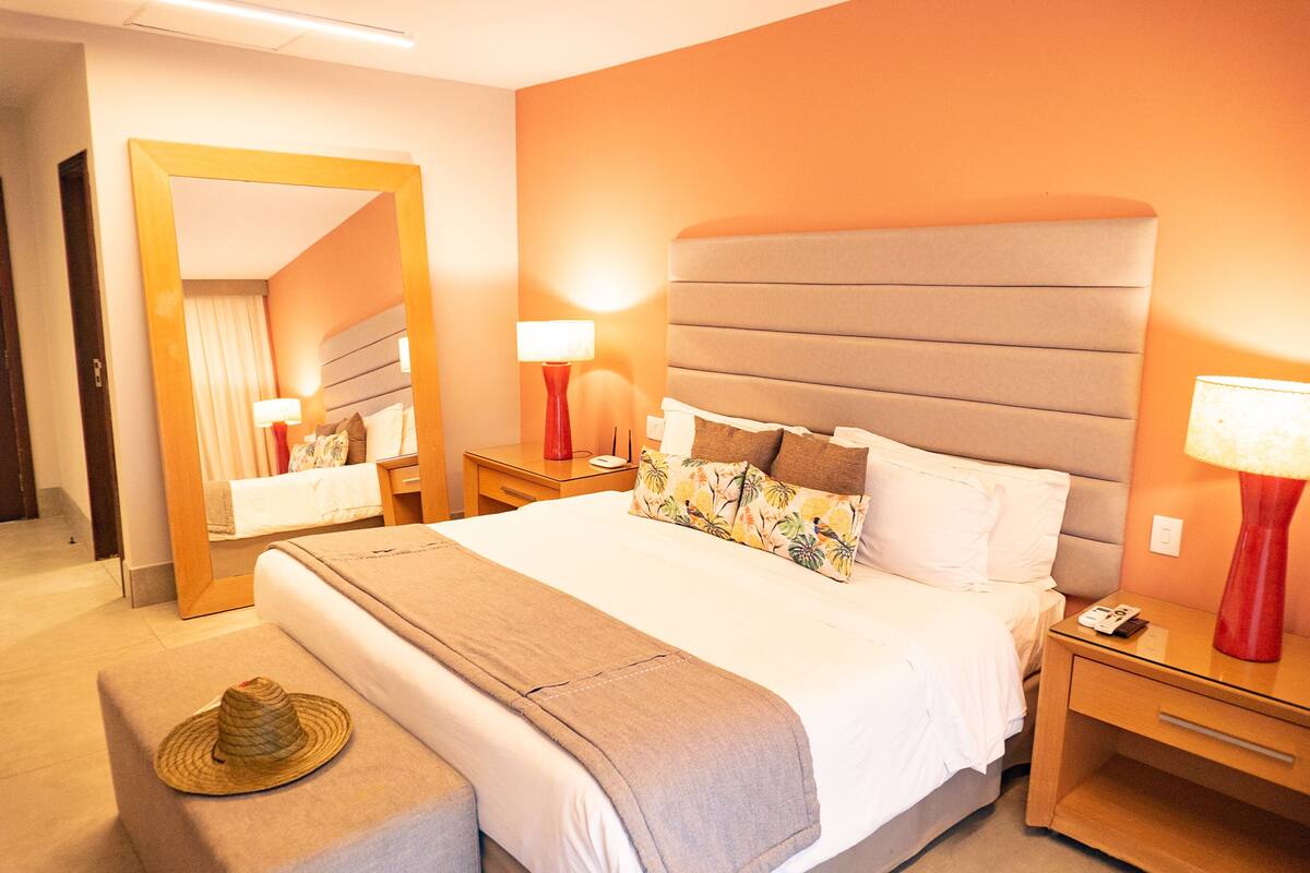 A hotel room with a large bed, a bedside table with a lamp, a nightstand, and a mirror.
