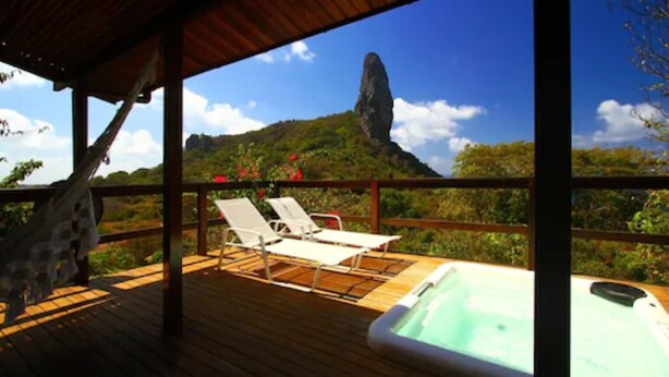 Een houten terras met lounge stoelen en een jacuzzi, met uitzicht op een bergachtig landschap.