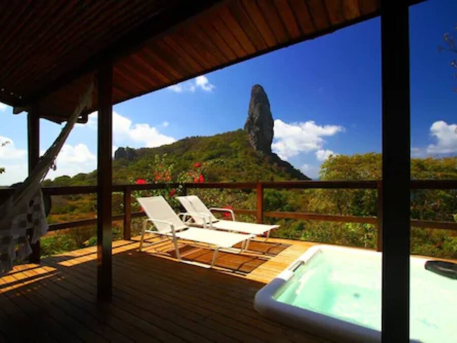 Terraza de madera con sillones de descanso y un jacuzzi, con vistas a un paisaje montañoso.