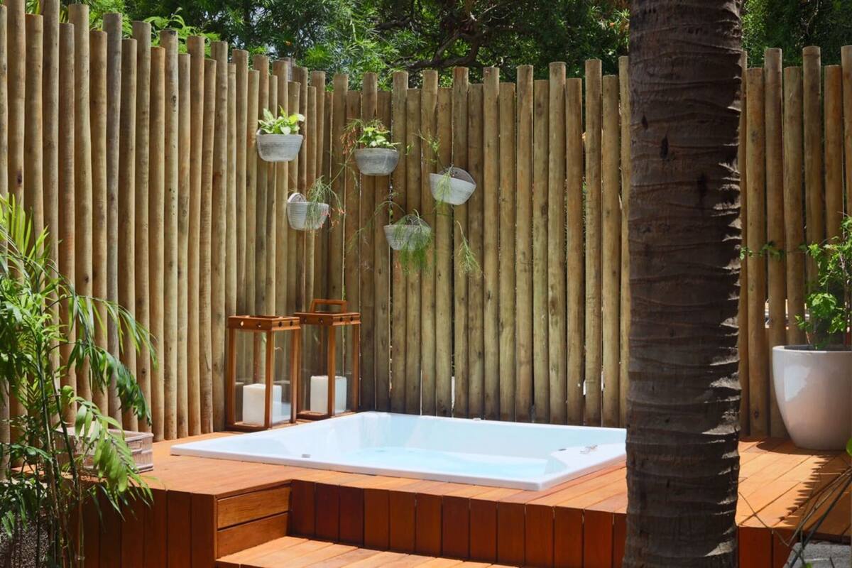 A wooden deck with a hot tub, surrounded by a bamboo fence and potted plants.