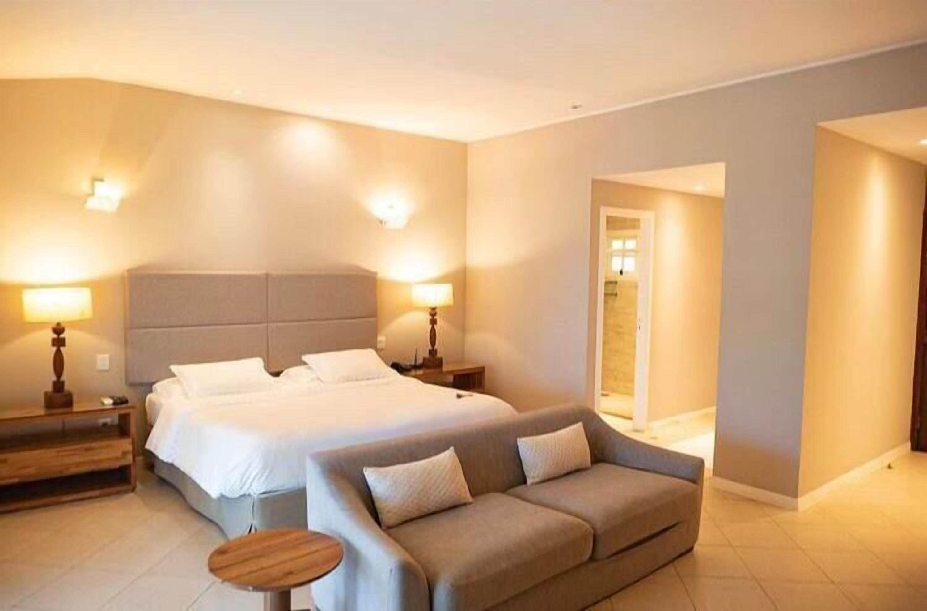 Ein Hotelzimmer mit einem großen Bett, zwei Nachttischen, einem Sofa und einem kleinen runden Tisch.