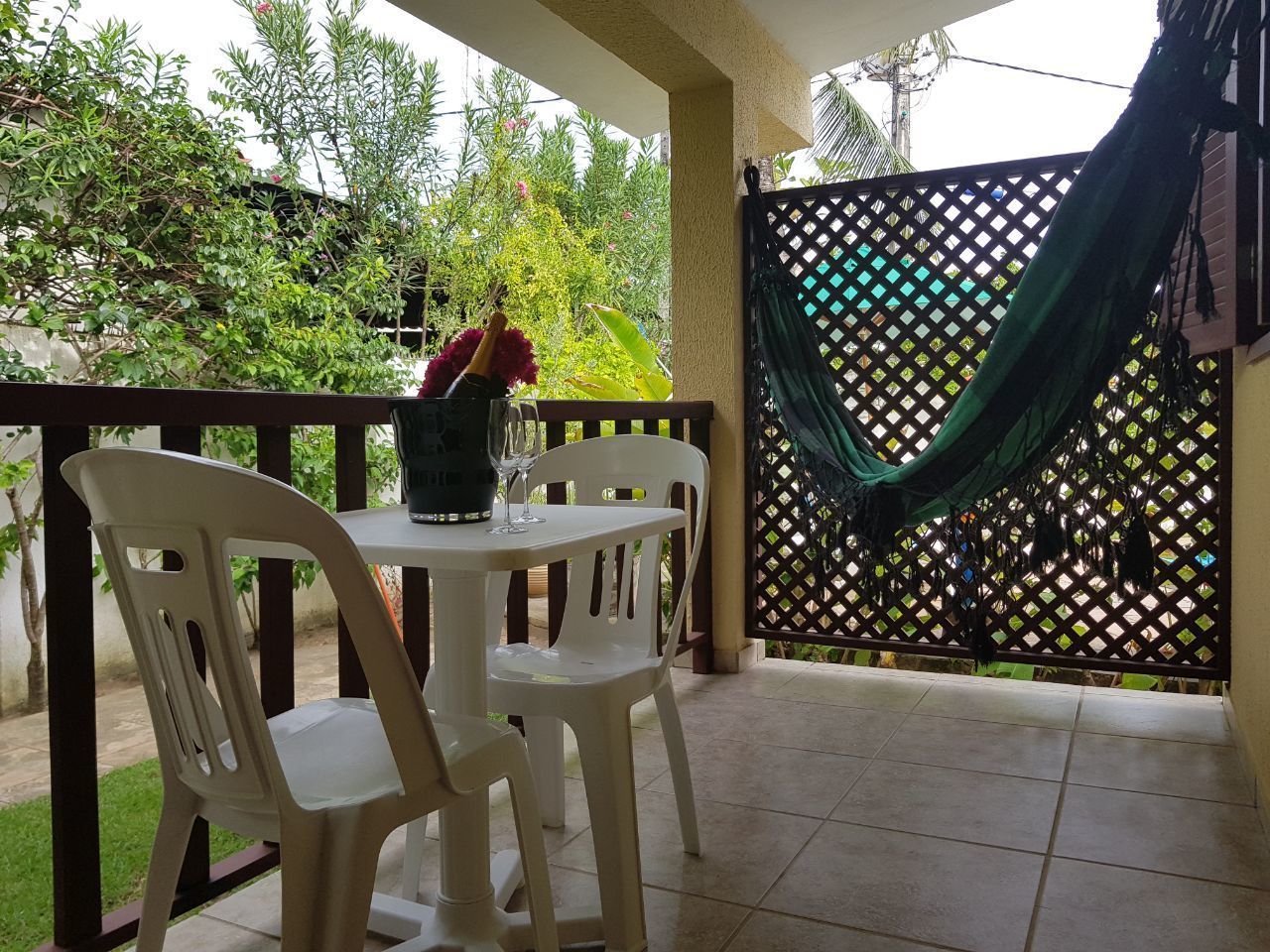 A covered patio area with a table and chairs, a hammock, and a view of greenery.