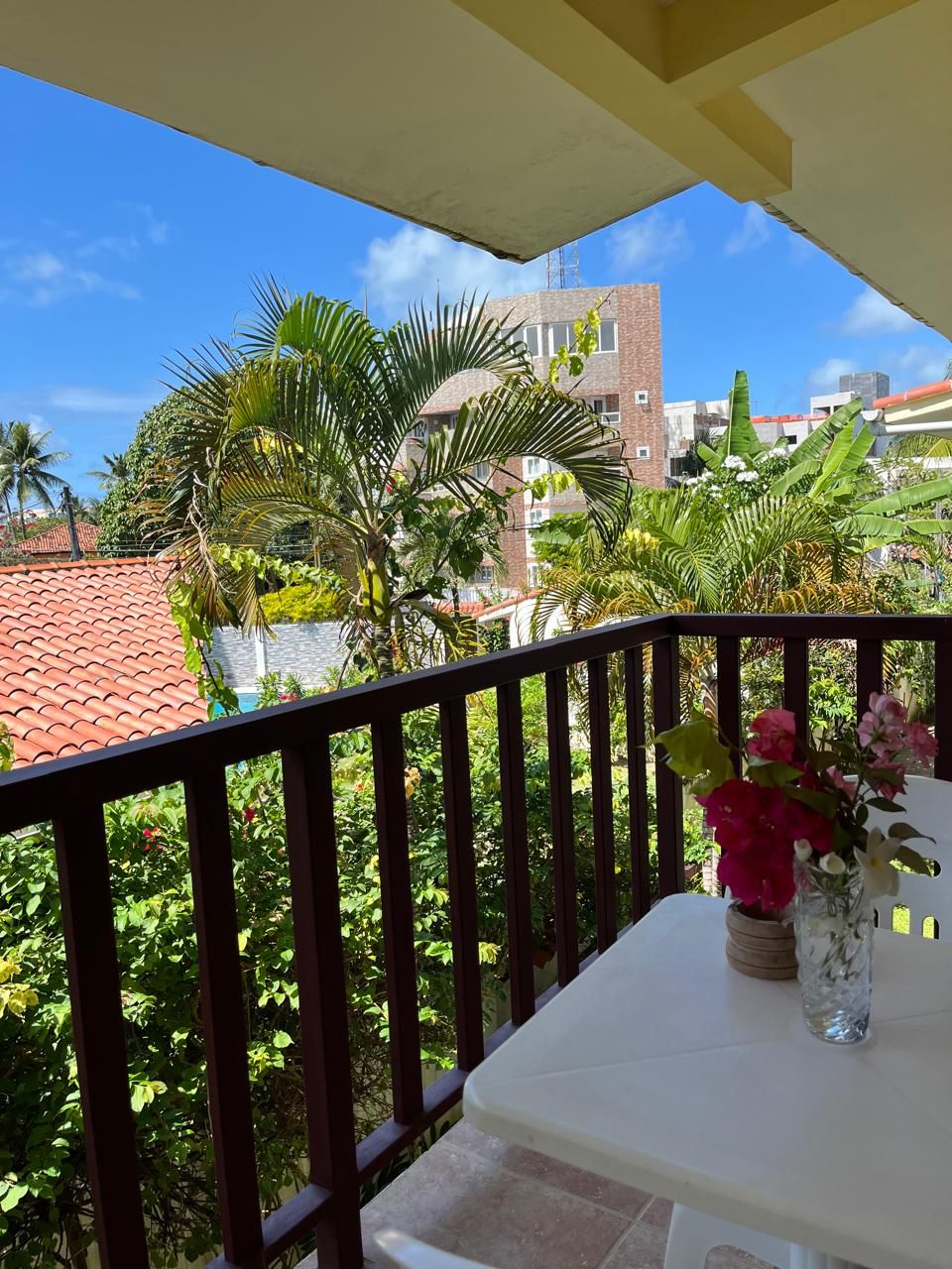 Un balcón con una mesa, un florero con flores y vistas a edificios y zonas verdes.