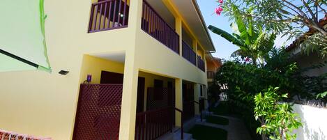 A two-story building with balconies, a covered walkway, and a garden area.