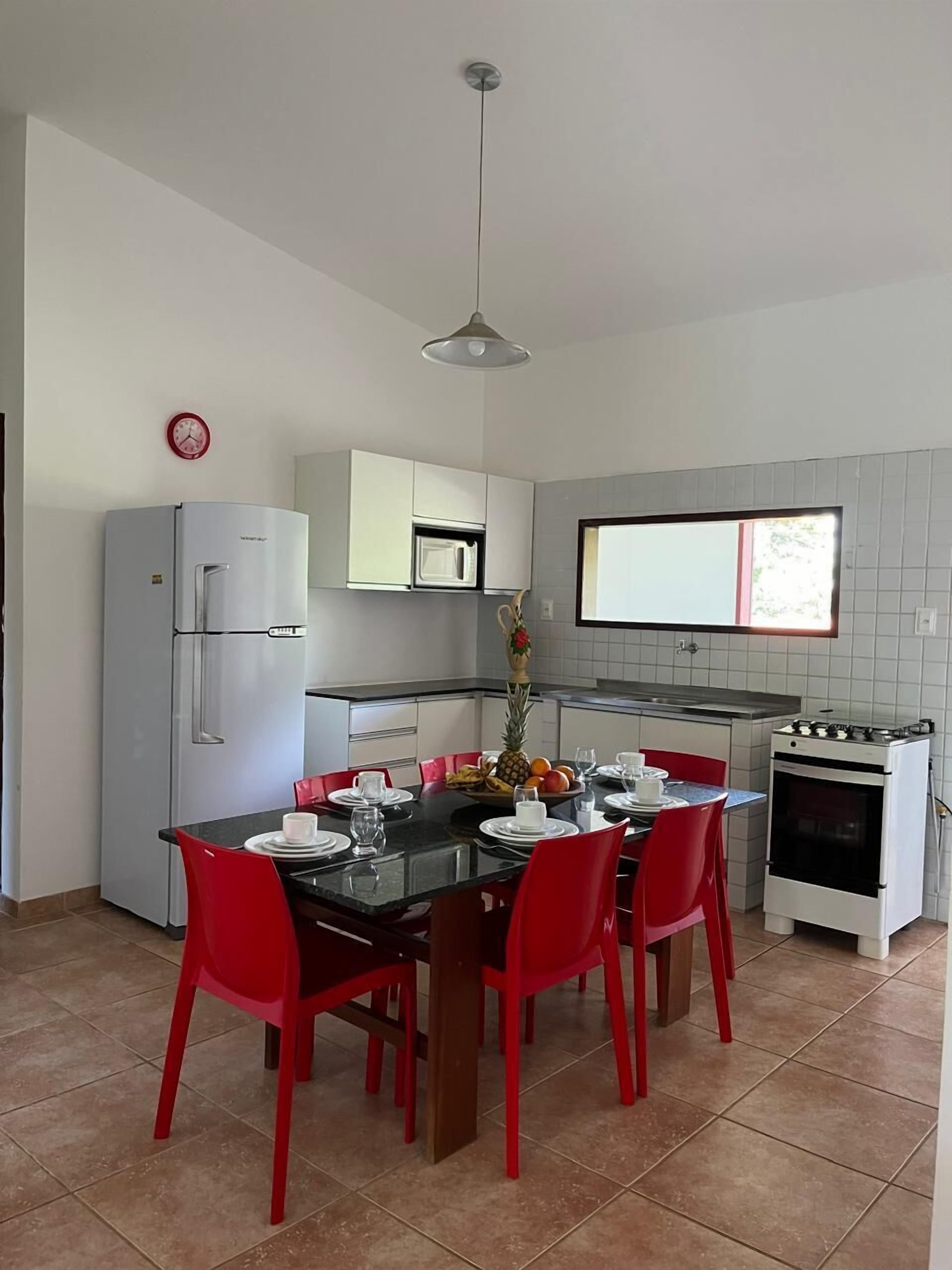 Cocina compacta con zona de comedor, que incluye refrigerador, microondas, estufa y una mesa de comedor lista para cuatro personas con sillas rojas.