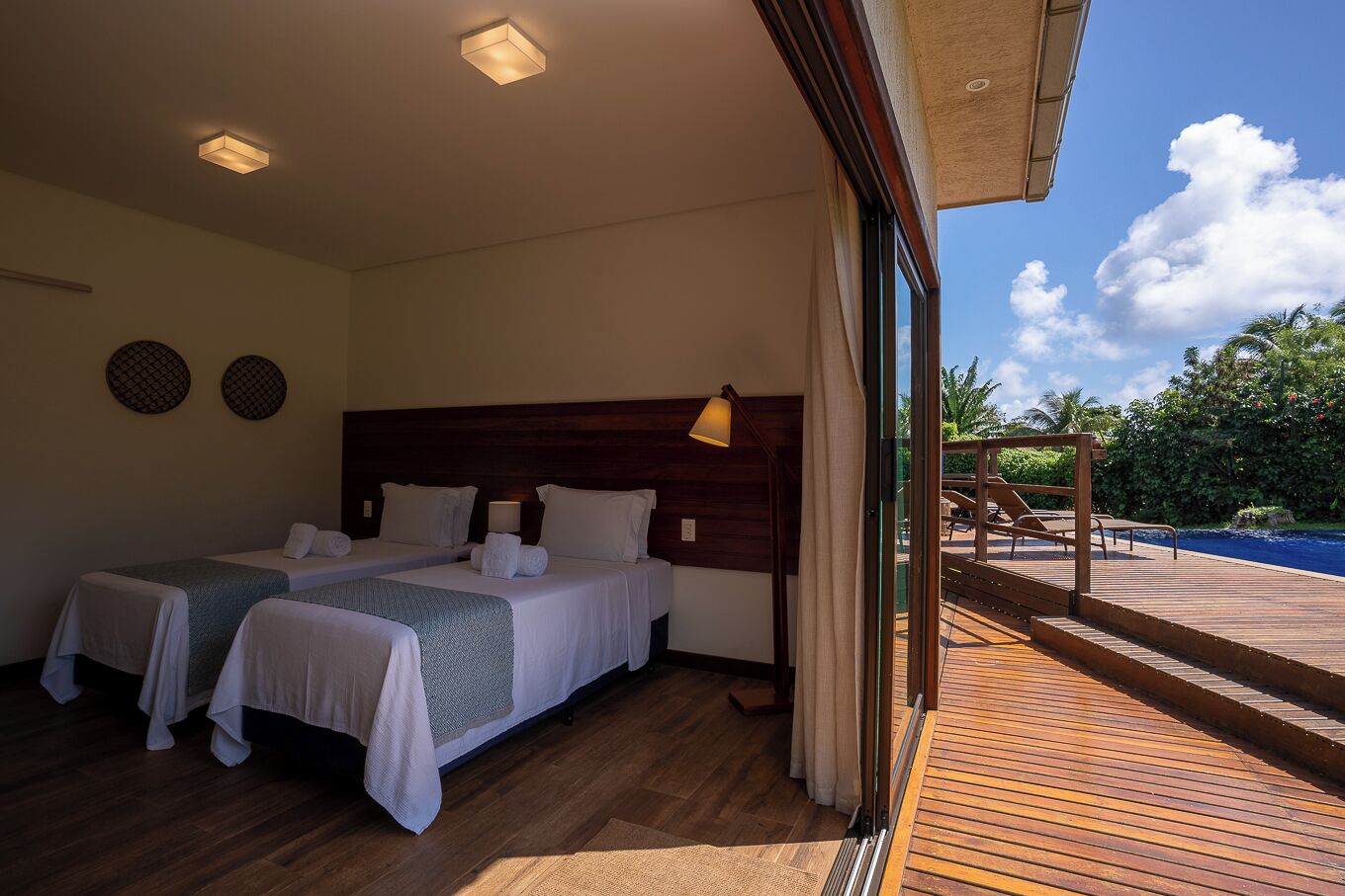 A hotel room with two beds, a wooden headboard, a large window, and a view of a pool and greenery outside.