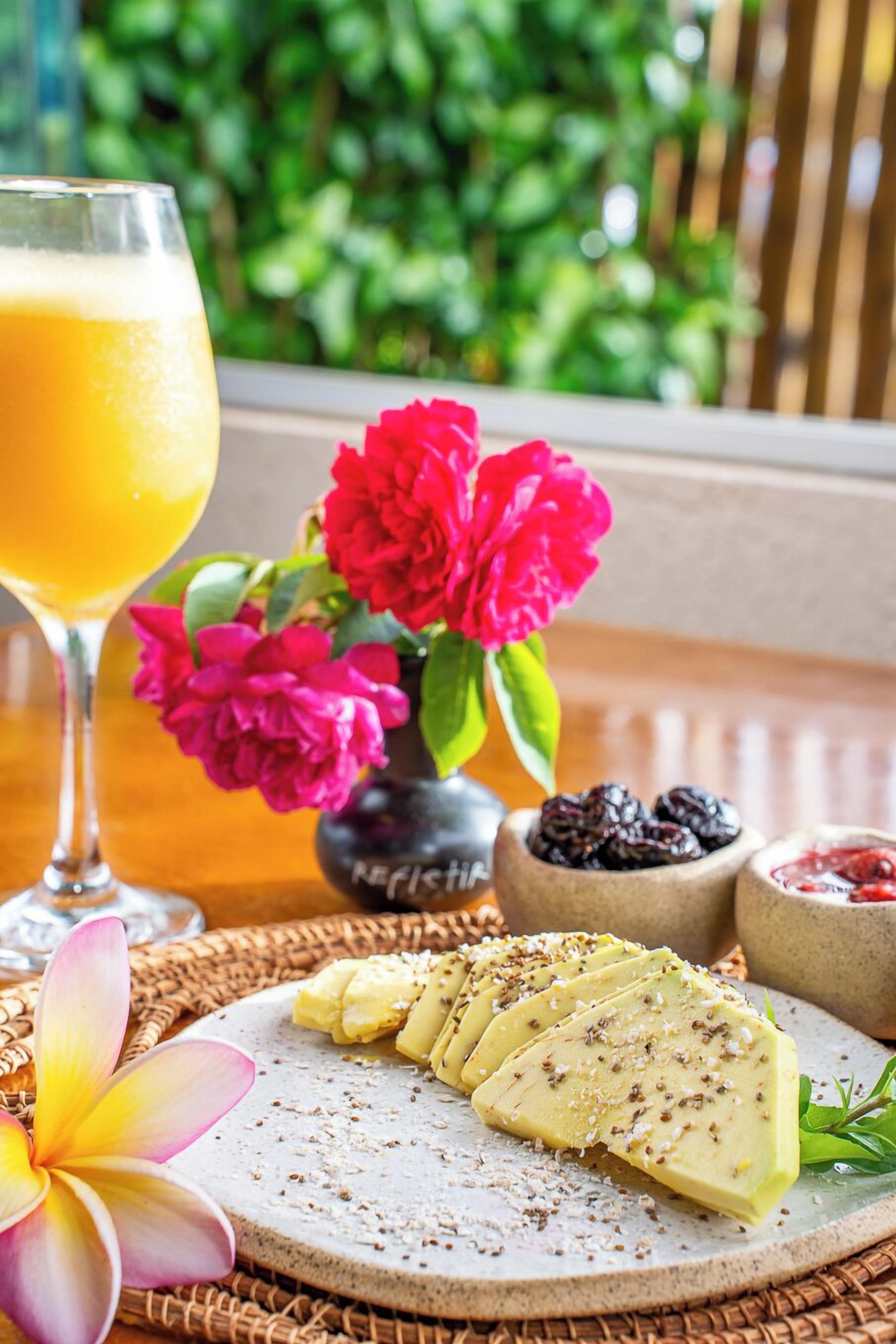 A table with a glass of orange juice, a plate of cheese, and a flower.