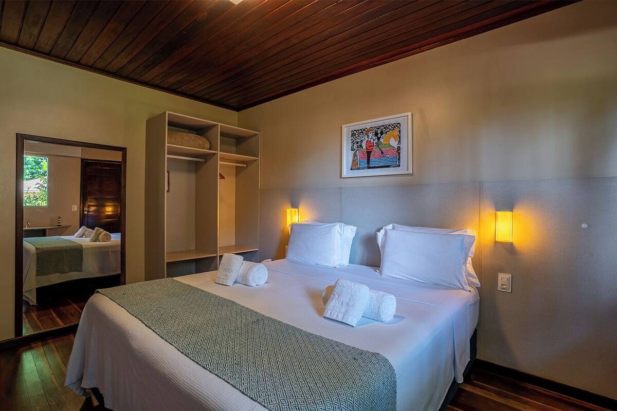 Quarto de hotel com uma cama grande, duas luminárias de cabeceira, um guarda-roupa e um espelho.
