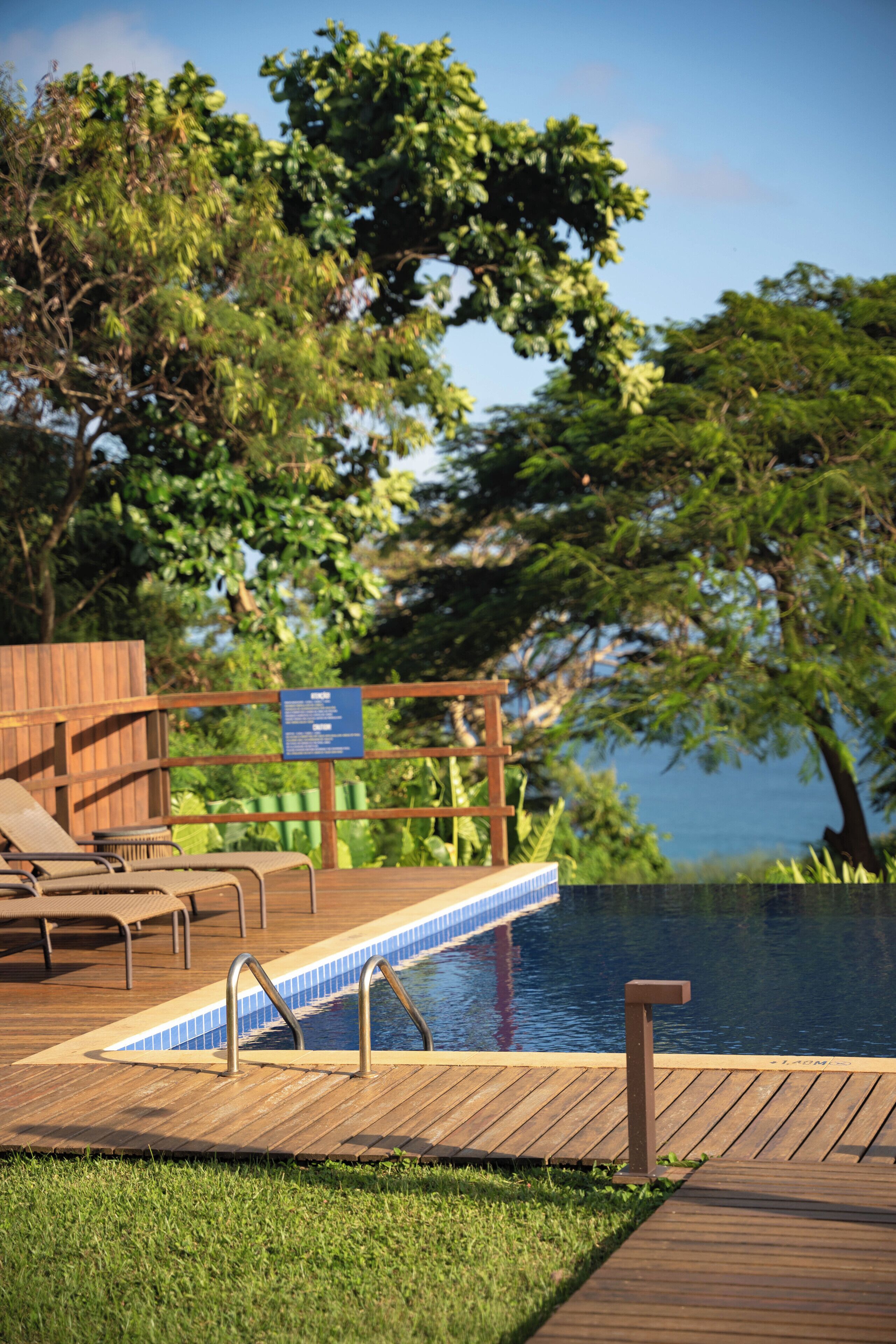 A wooden deck with a pool, lounge chairs, and a sign.