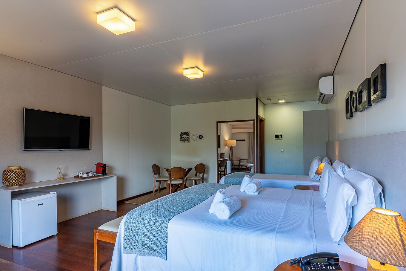 Et hotelværelse med seng, natbord, lampe, fjernsyn, skrivebord, stol og et lille tekøkken.