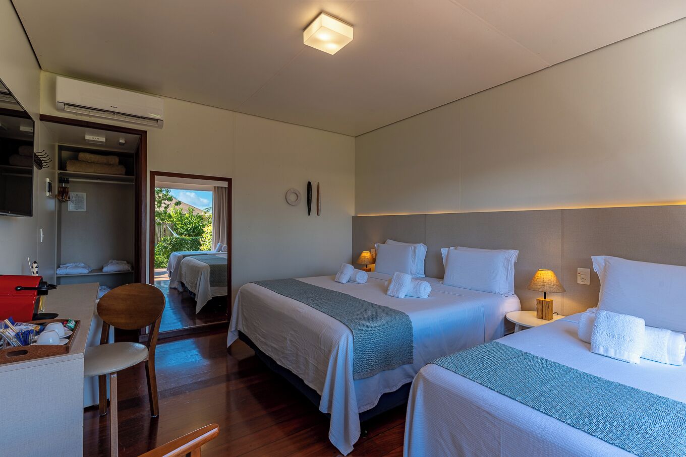 A hotel room with two beds, a desk, a chair, and a view of the outdoors.