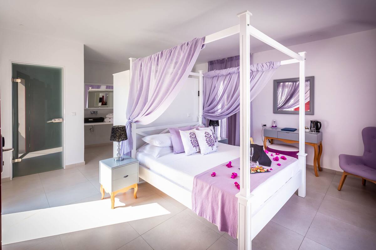A bedroom with a four-poster bed, a nightstand, a desk, and a chair.