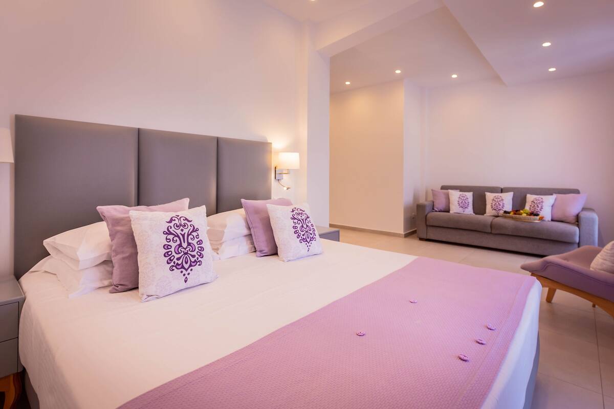 A modern hotel room with a large bed, a sofa, and a nightstand.