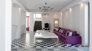 Uma sala de estar moderna com piso xadrez, mesa de centro branca, sofá roxo e um lustre.
