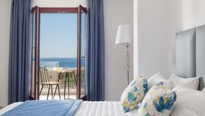 Quarto de hotel com cama, uma cadeira, uma mesa e vista para o mar.