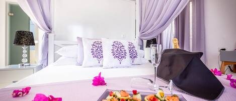 A hotel room with a bed, a bedside table with a lamp, and a tray with food and a glass of water.