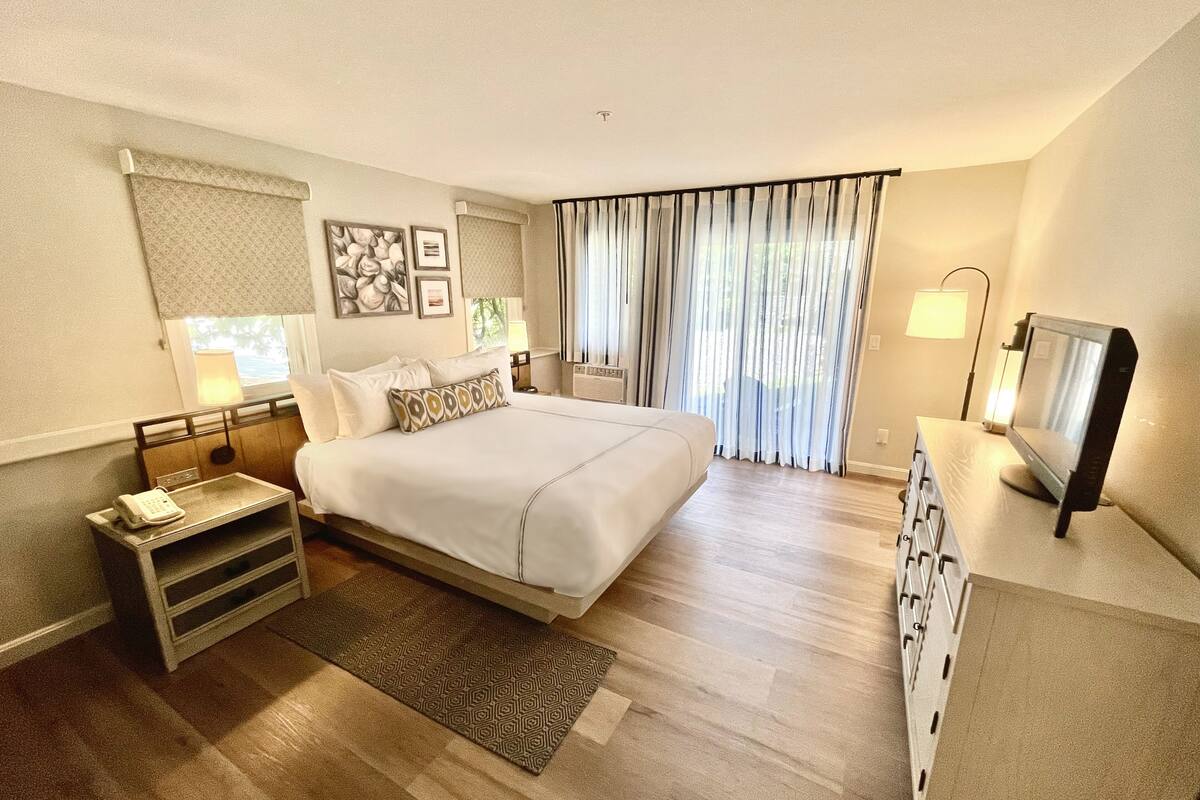 A hotel room with a large bed, bedside tables, a desk, a TV, and a window with curtains.