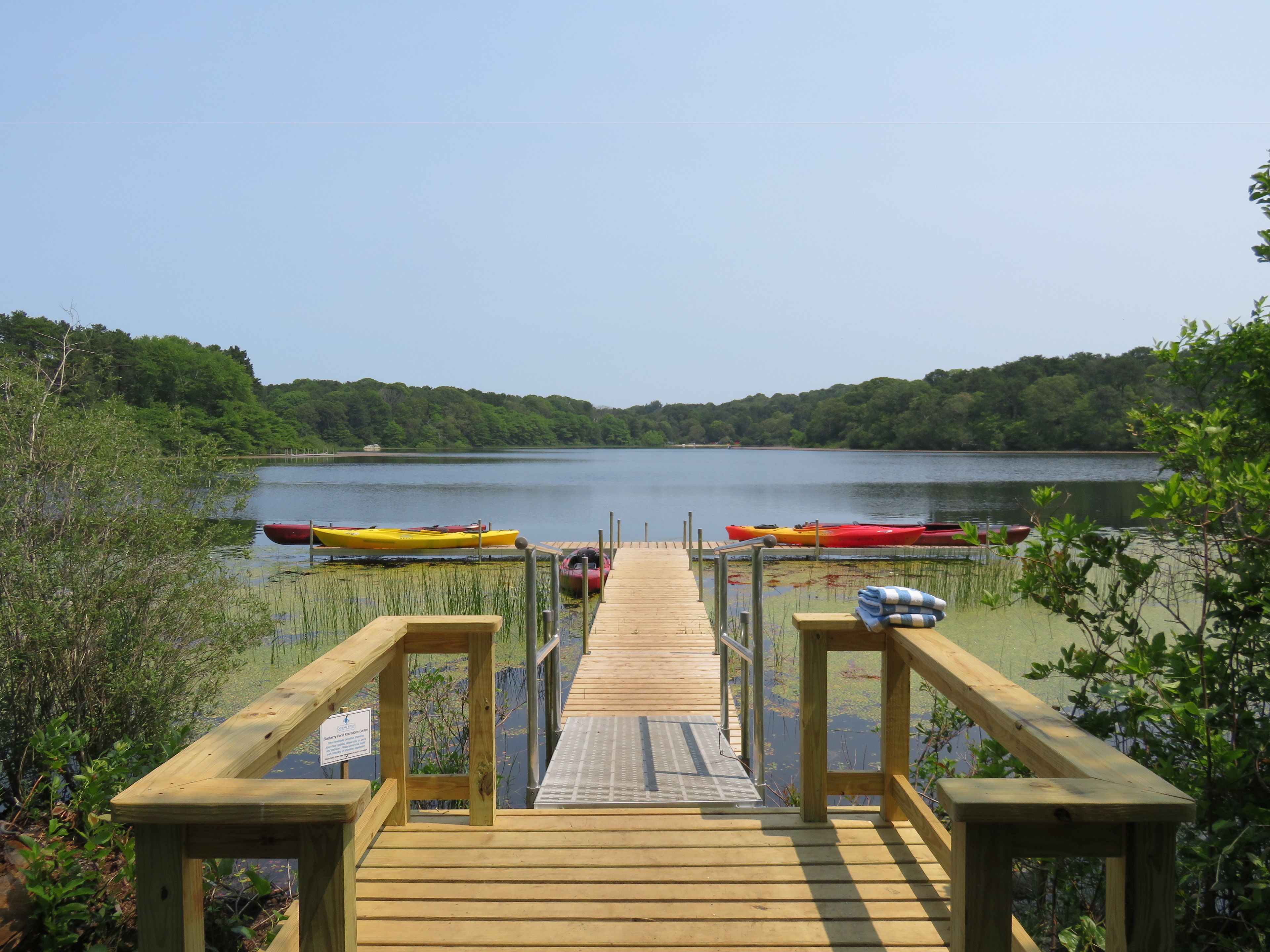 A wooden dock leading to a lake with several kayaks and canoes docked at the far end.