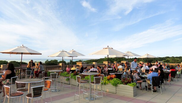 An outdoor patio with tables and chairs, umbrellas, and a view of the ocean. - The Villages at Ocean Edge (Brewster)