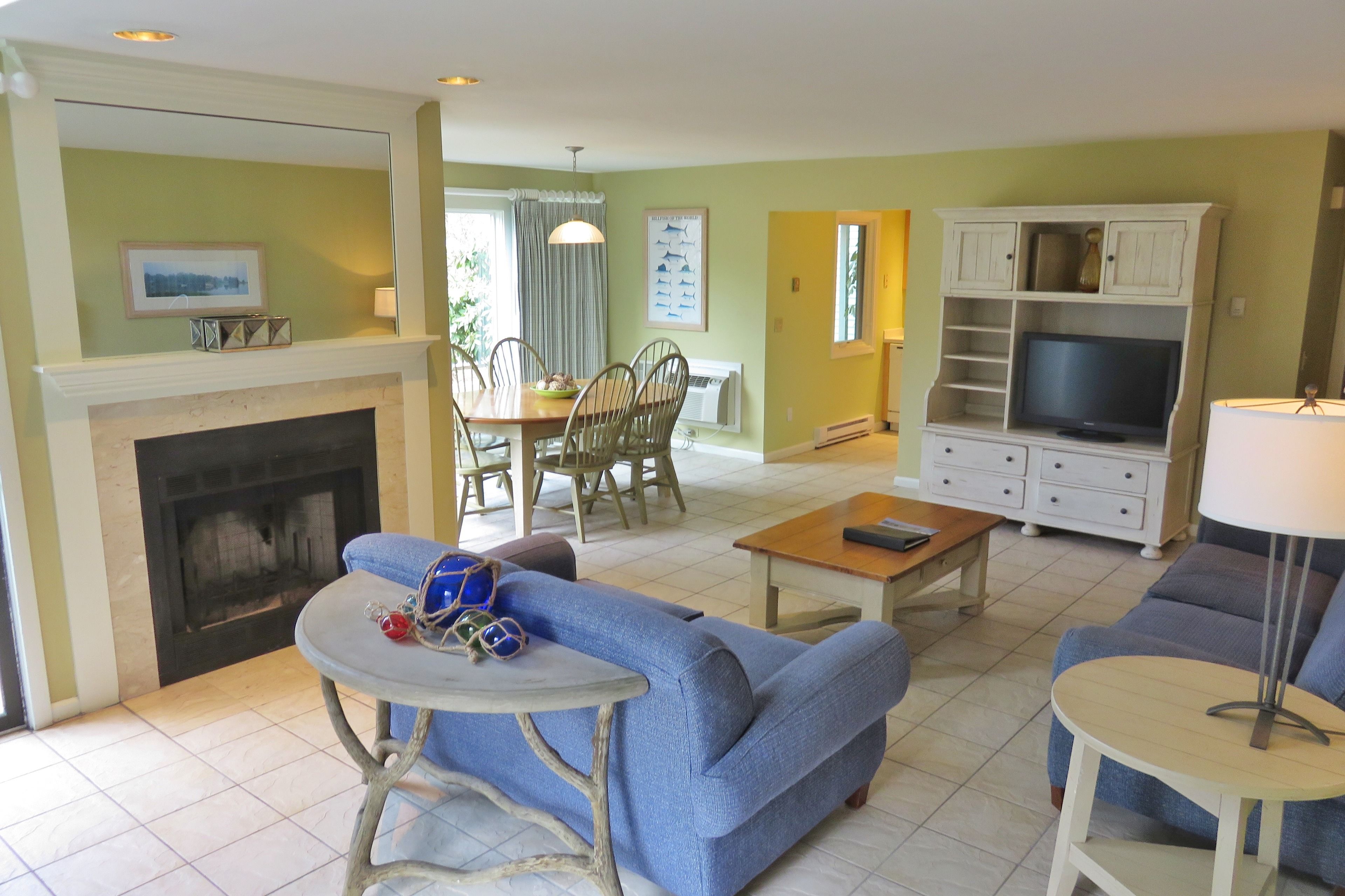 A living room with a fireplace, blue sofa, dining table, and TV stand.