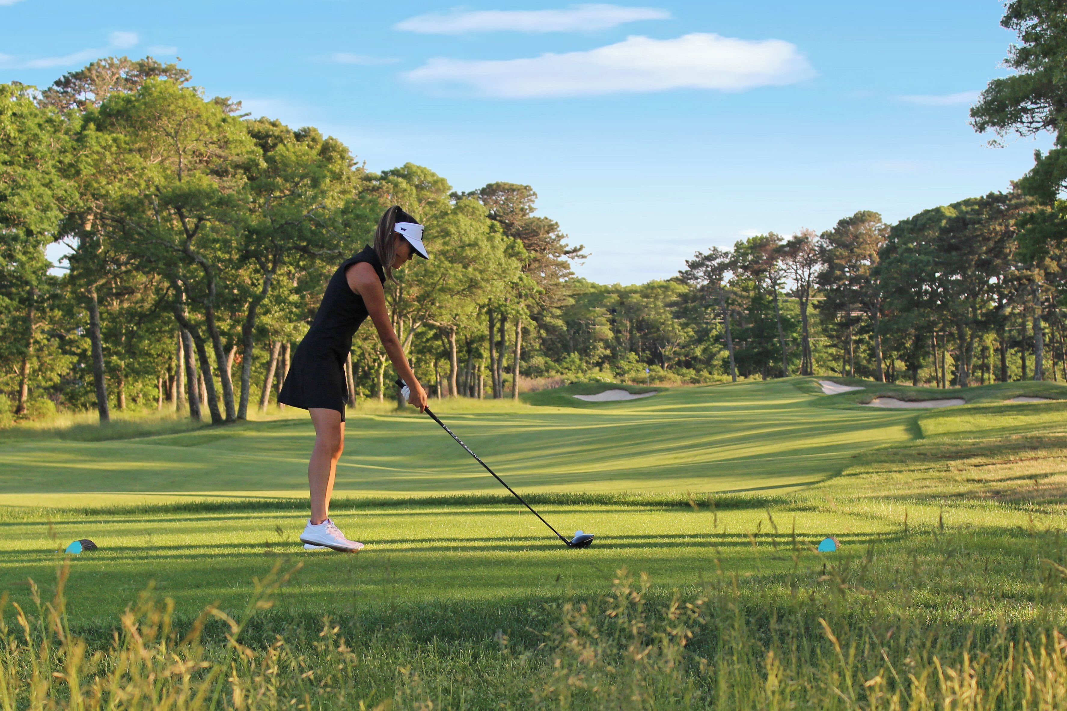 Une personne jouant au golf sur un parcours bien entretenu, avec des arbres en arrière-plan.