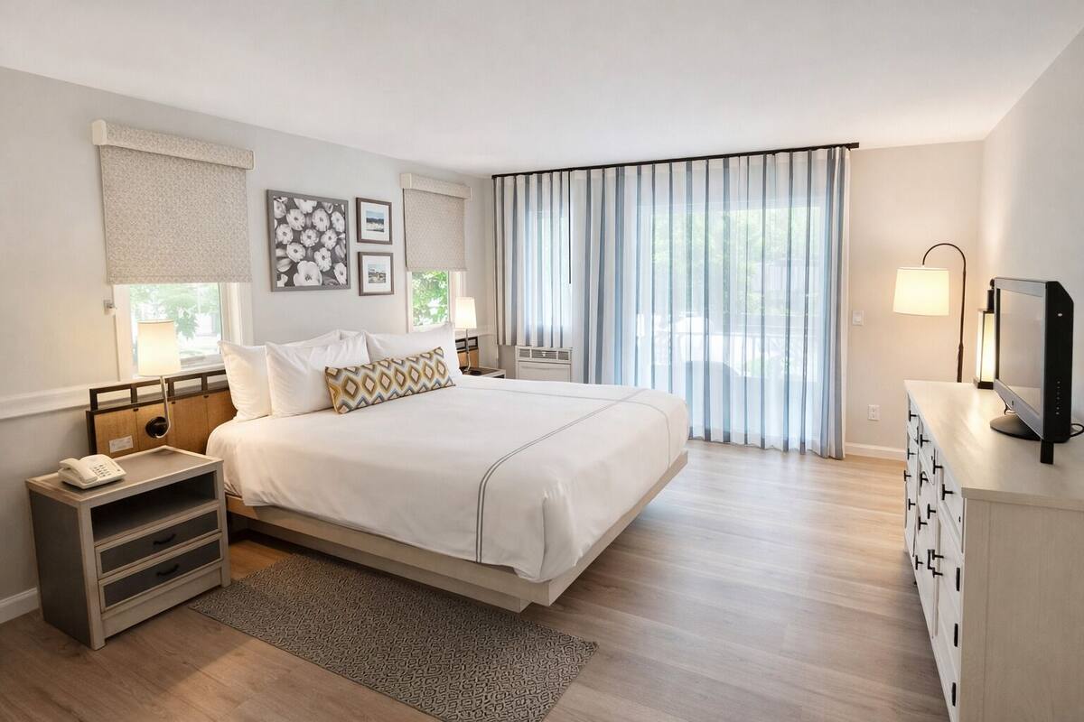A modern hotel room with a large bed, bedside tables, a desk with a computer, and a large window with curtains.