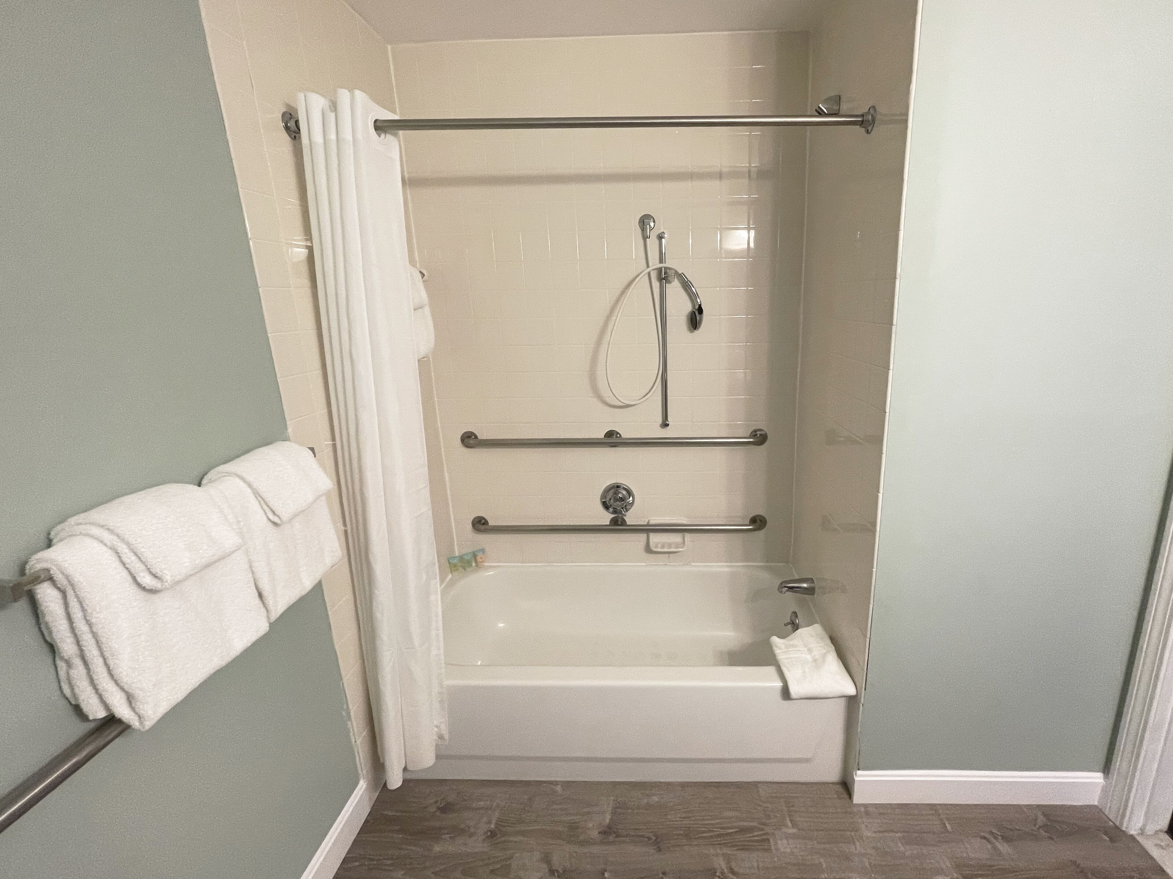 Une douche à l’italienne avec une porte en verre, une barre d’appui et une douchette amovible.