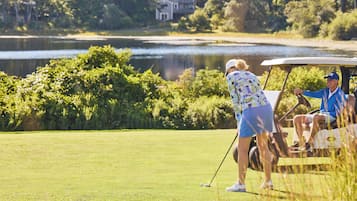 A golf course with a water body in the background, a house, and dense greenery.