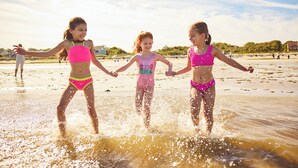 Three children playing in shallow water on a beach. - The Villages at Ocean Edge (Brewster)