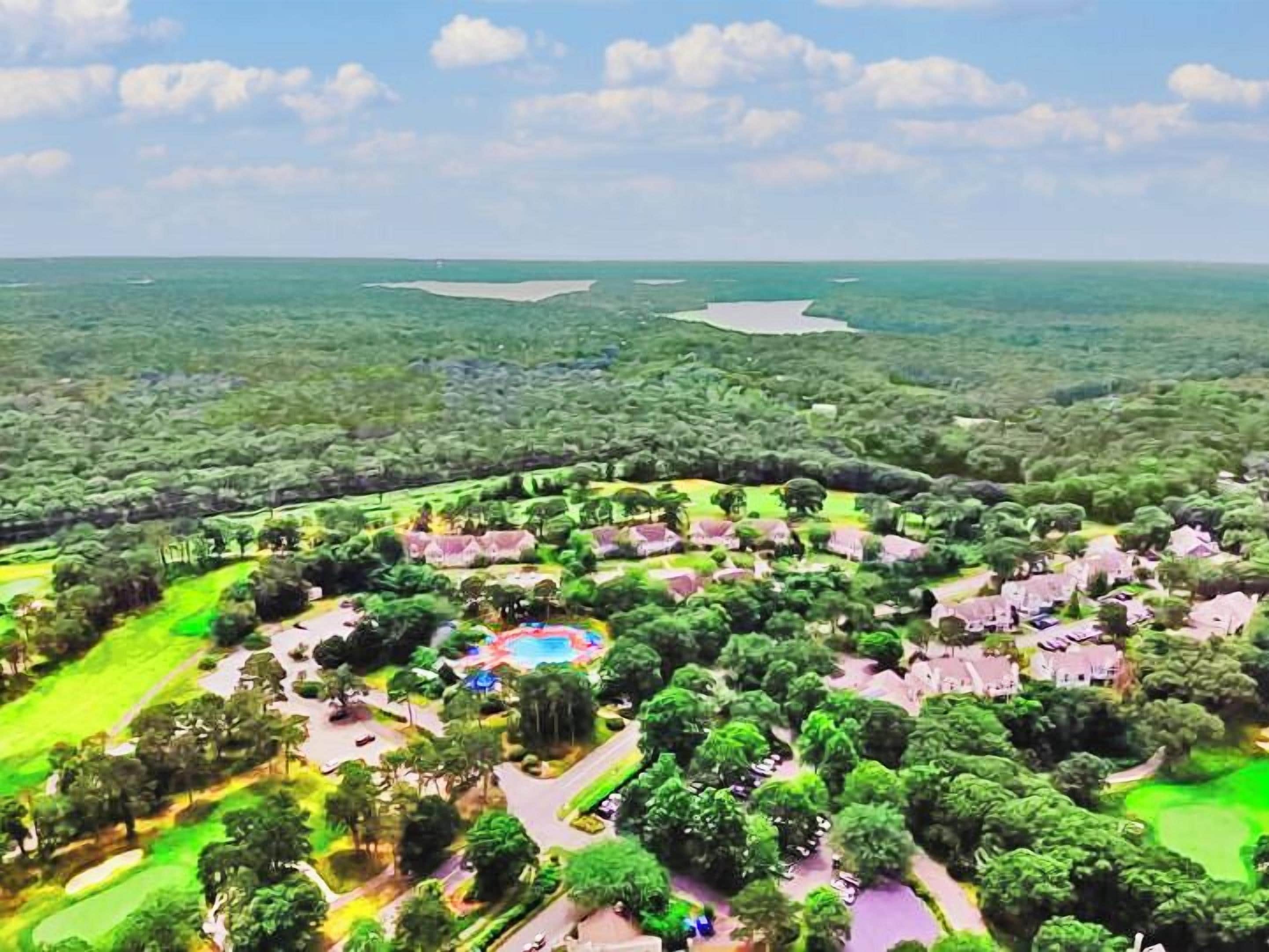 Vista aérea de un resort con varias edificaciones, una piscina central y follaje circundante.