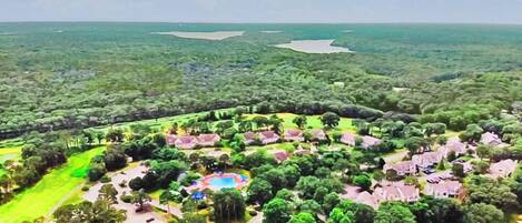 Vista aérea de un resort con varias edificaciones, una piscina central y follaje circundante.
